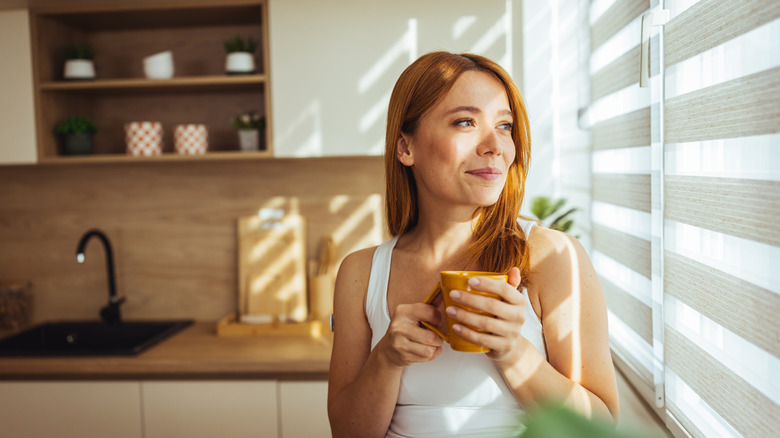 Woman staring out a kitchen window with blinds