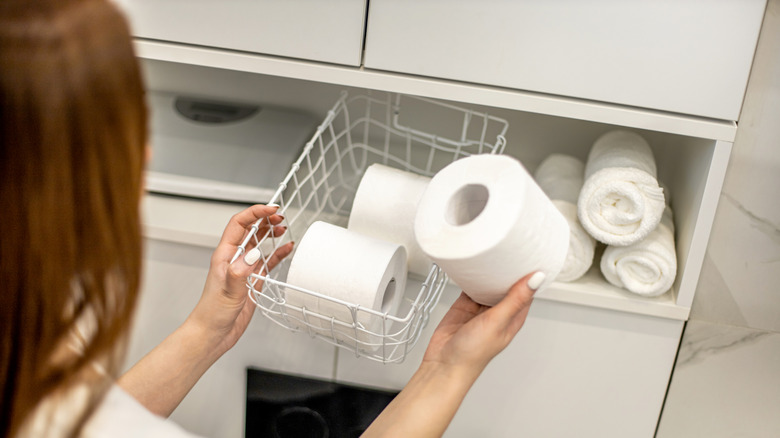 Person putting toilet paper rolls in a white wire basket
