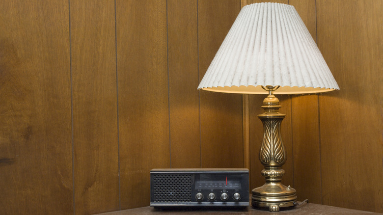 A vintage metal lamp with a fluted white lampshade against a paneled wood wall
