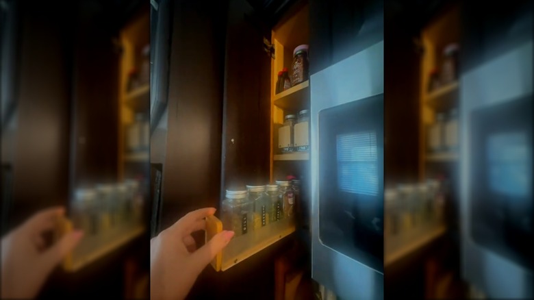 Woman using pull-out spice organizer in narrow cabinet