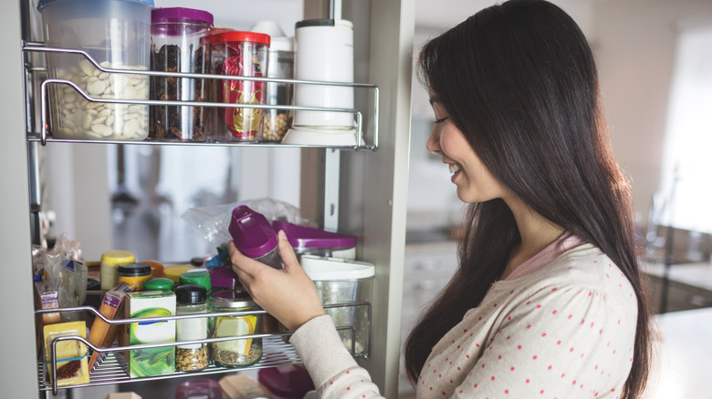 Woman taking a spice jar from a cabinet