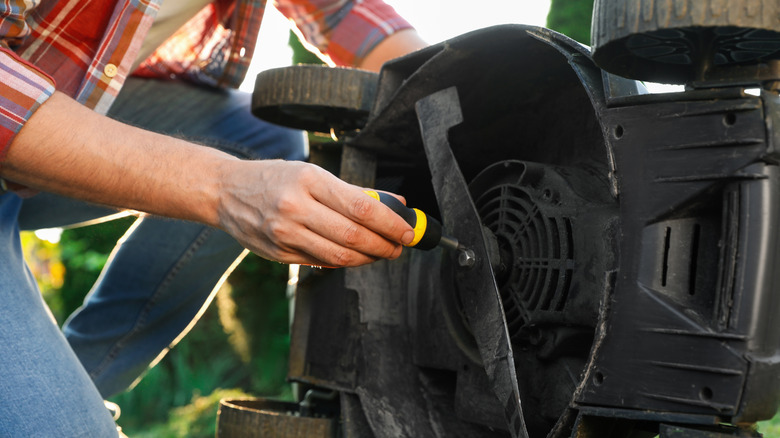 A man takes the blade off of a lawnmower