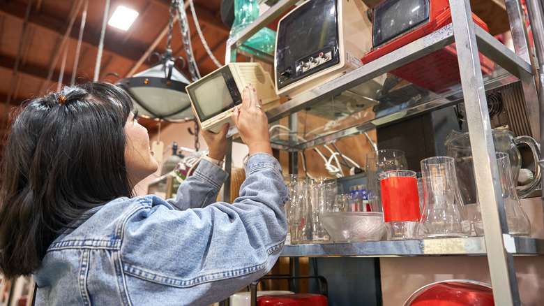 Woman reaching for an old miniature TV in an antique store