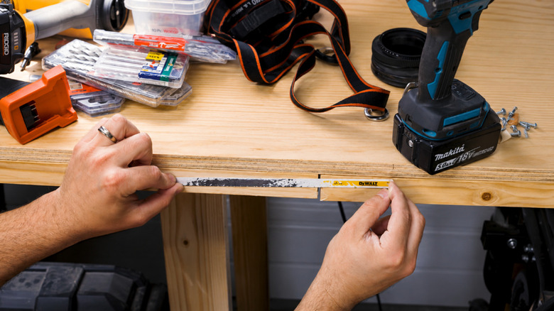 Person nailing a hacksaw blade to the edge of a worktable