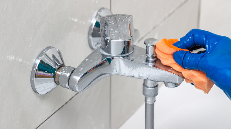 A gloved hand cleaning a bathtub